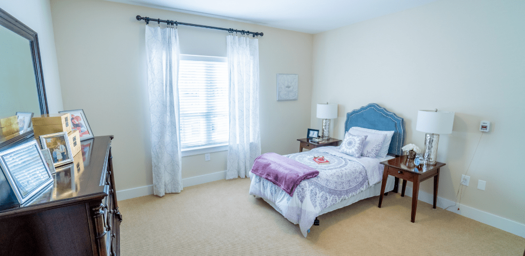 A bright and cozy bedroom with a single bed, nightstand, and window with translucent curtains.