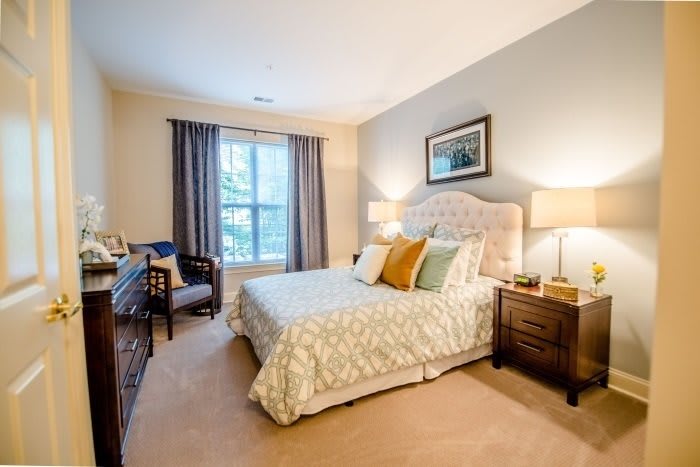 A cozy and well-decorated bedroom featuring a comfortable bed, elegant lamps, and a window with drapes.