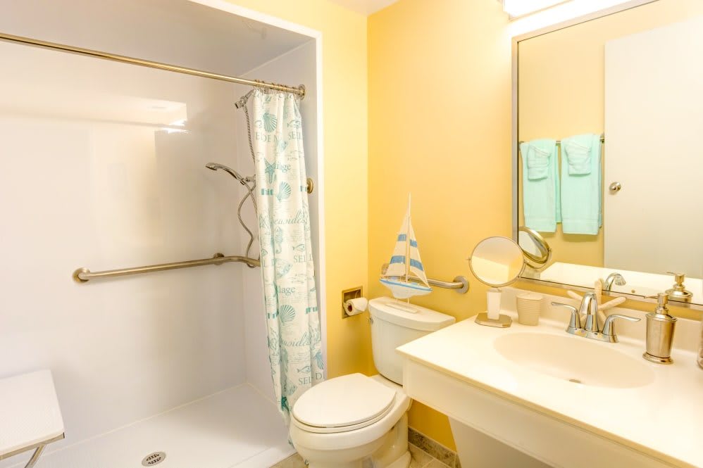 A clean and bright bathroom with a shower, toilet, sink, and mirror.