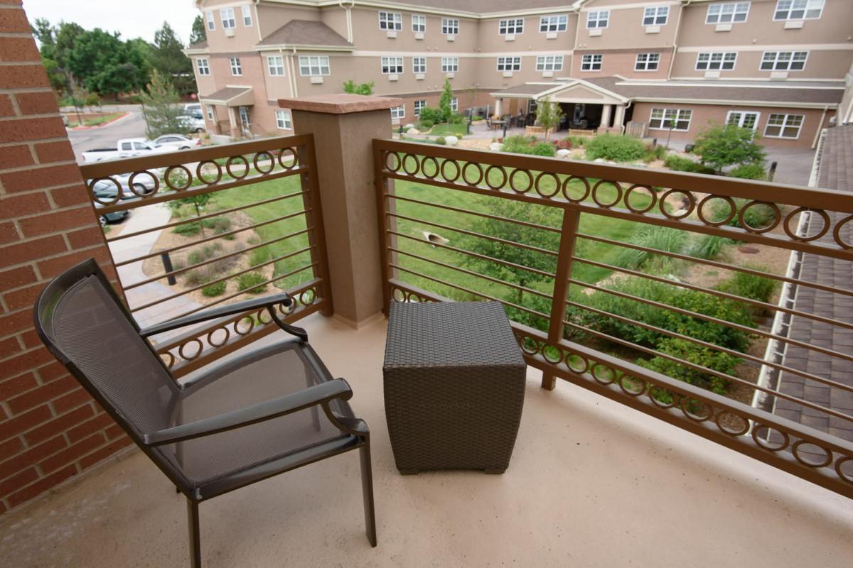 A balcony overlooking a garden with two chairs and a table.