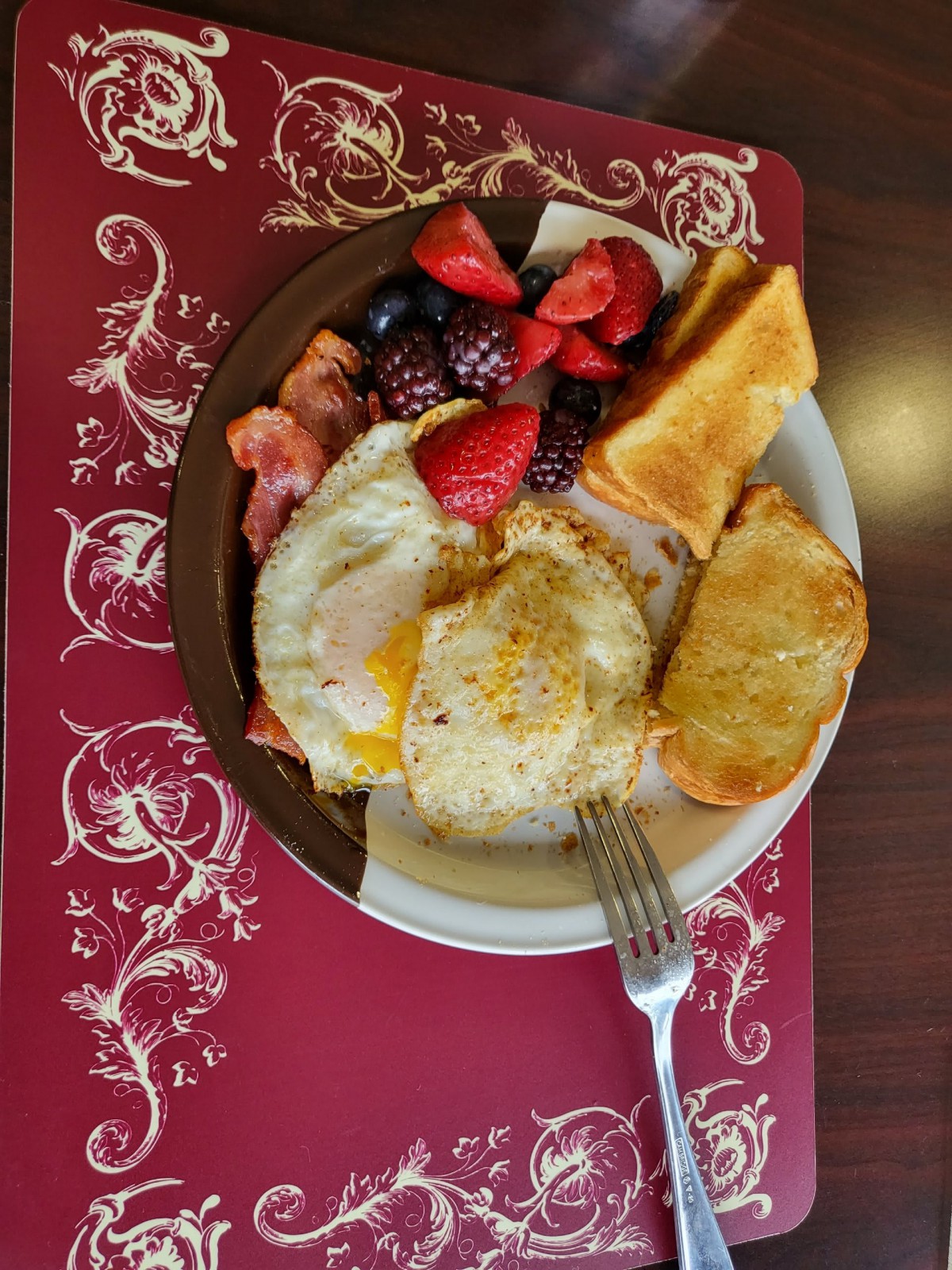 A hearty breakfast plate featuring eggs, bacon, toast, hash browns, and fresh fruit.