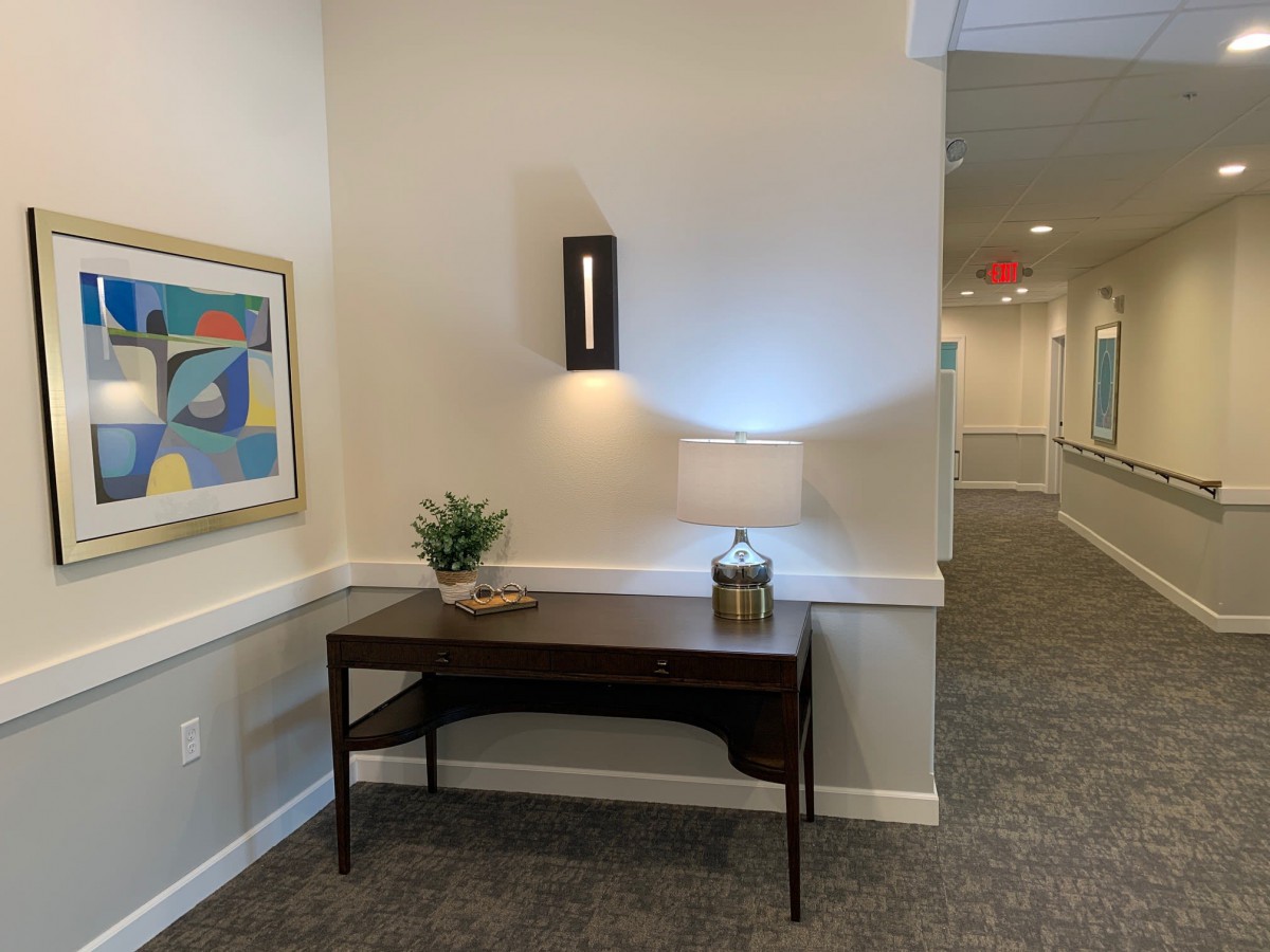A well-decorated hallway featuring a table with a lamp, artwork on the wall, and a small plant for decoration.