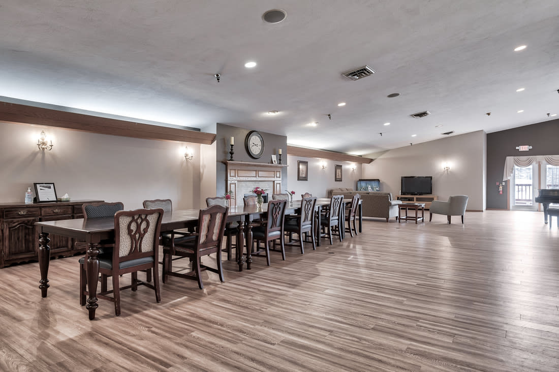 A spacious dining room with long wooden tables and chairs, featuring a fireplace and wood flooring.