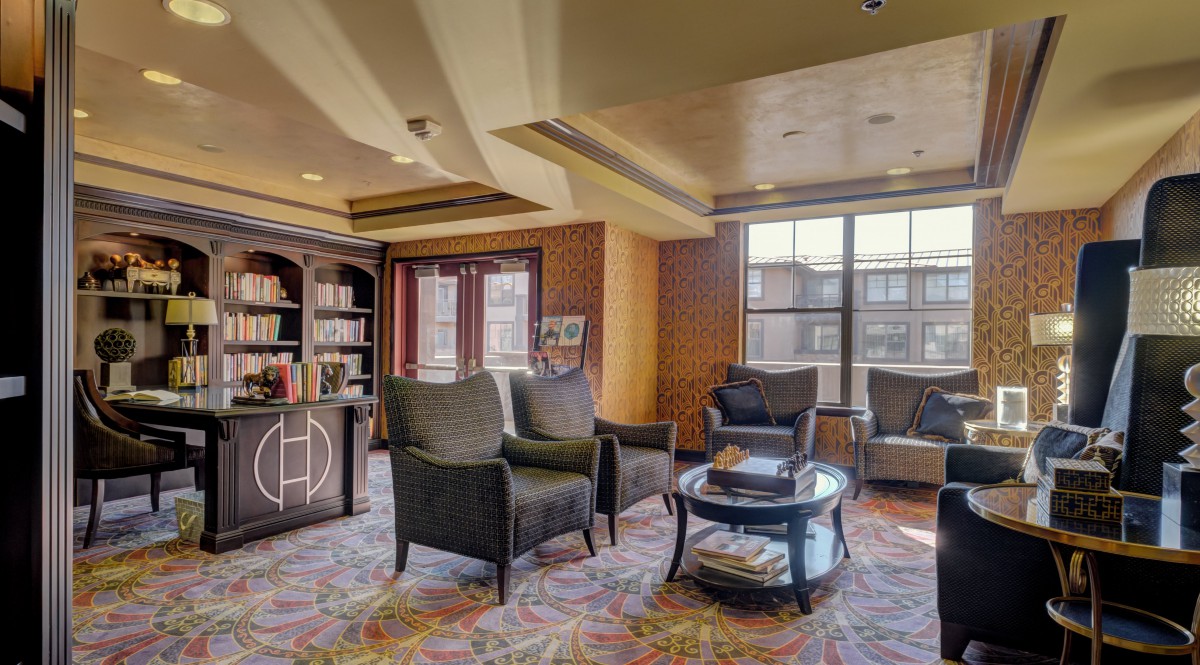 A cozy lobby seating area with armchairs, a round table, and a bookshelf against large windows.
