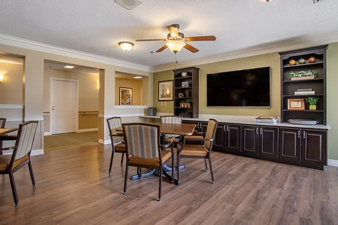 A cozy living space featuring a dining area with four chairs, a large television mounted on the wall, and elegant wood flooring.
