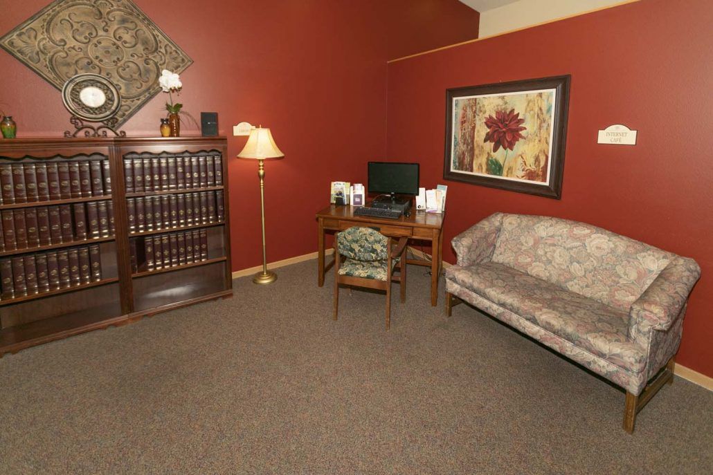A cozy office space with a bookshelf, desk, lamp, and sofa set against red walls.