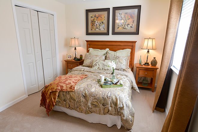 A cozy bedroom with a neatly made bed, flanked by two bedside tables and lamps, decorated with framed artwork above the headboard.