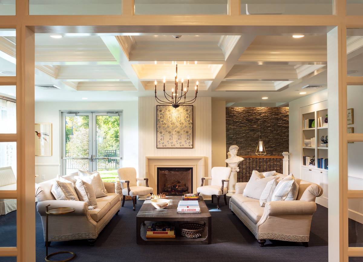 A modern and cozy living room featuring a fireplace, elegant chandelier, and comfortable seating arrangements with large windows providing ample natural light.