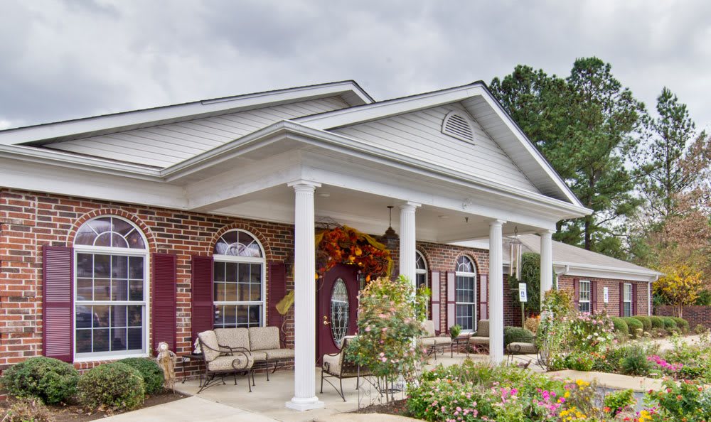 A charming brick house featuring a porch with columns, surrounded by well-maintained landscaping and flower arrangements.