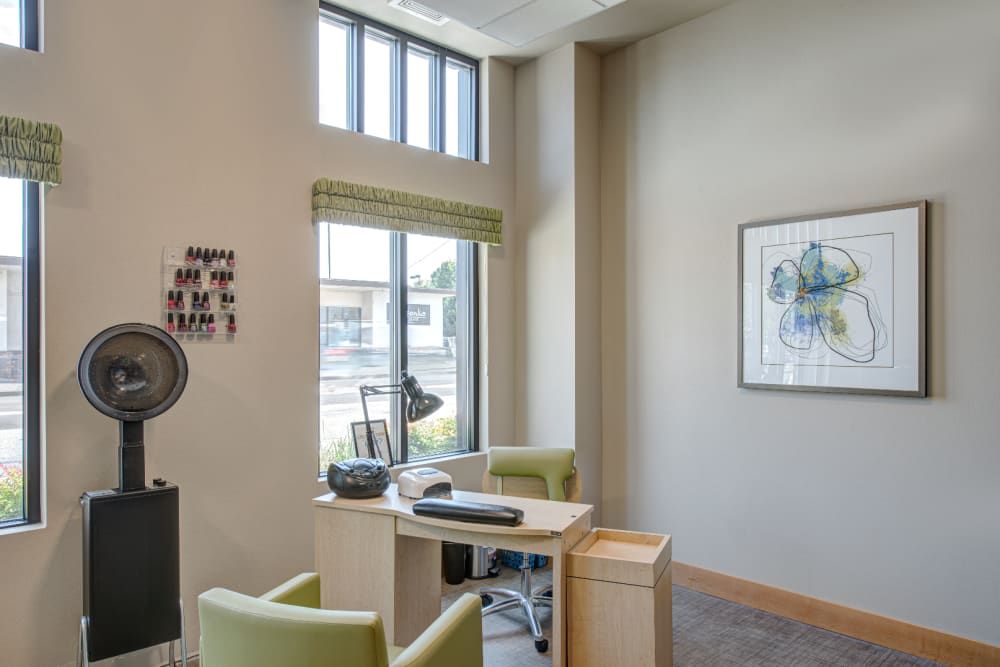 A modern office space with a desk and chairs, featuring large windows and wall art.