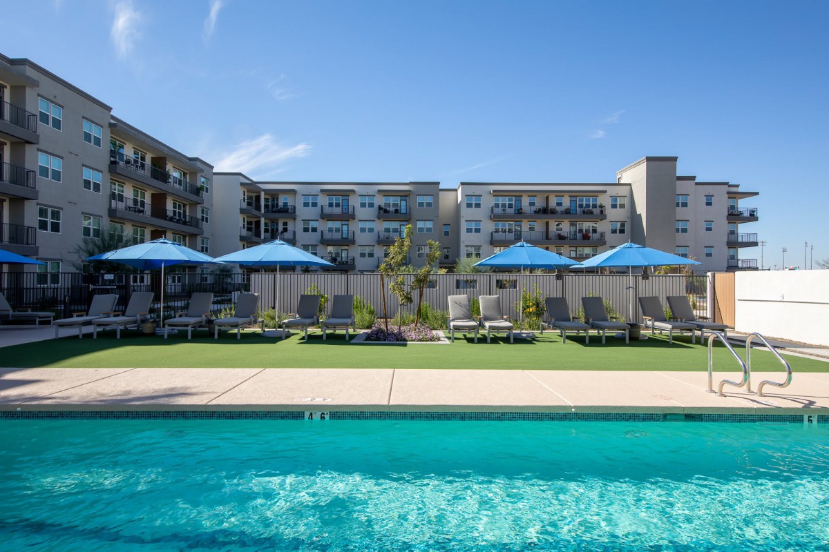 A sunny day at a hotel resort featuring a swimming pool, lawn chairs, and blue umbrellas.