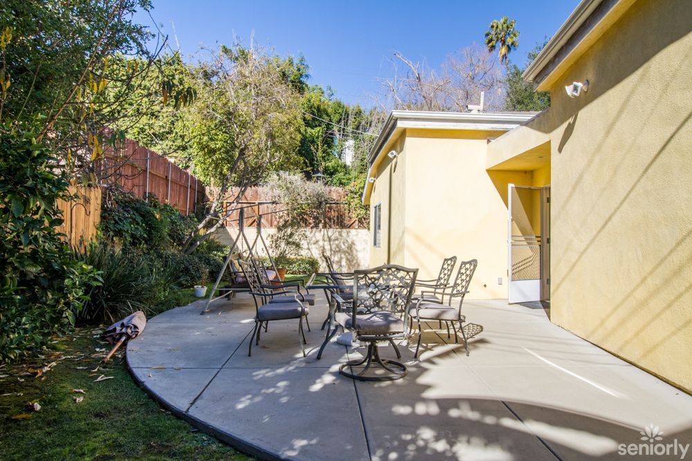 A sunny backyard patio with outdoor furniture and lush greenery.
