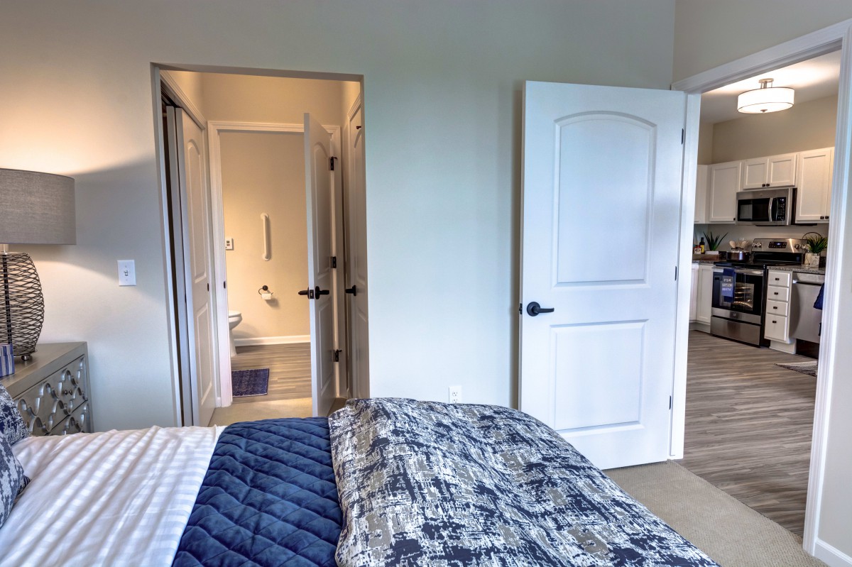 A cozy bedroom with a view into an adjacent bathroom, featuring a bed with patterned blankets and open doors.