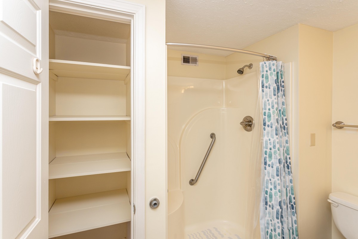 A bathroom featuring a shower with a grab bar and adjacent shelving.