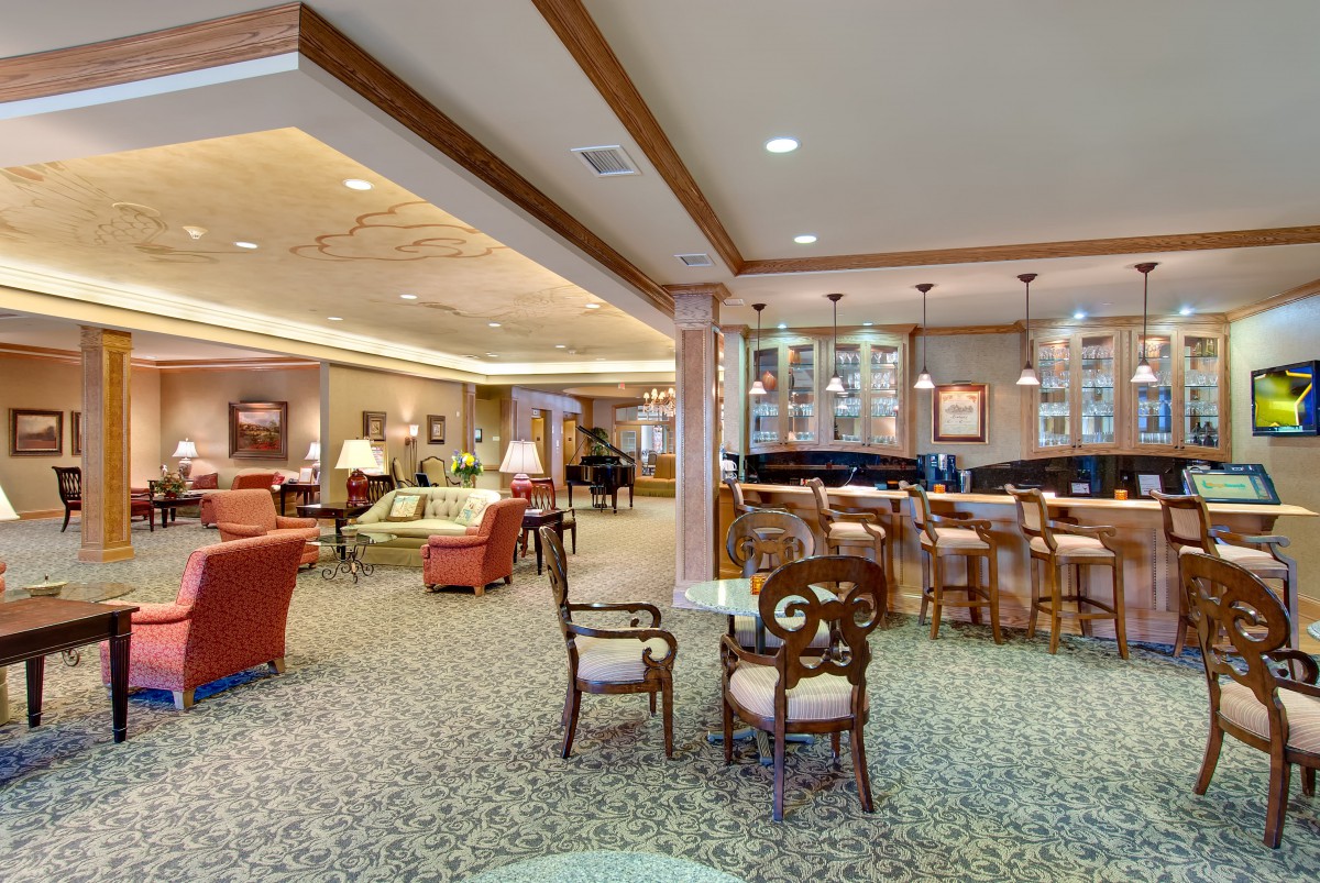 A cozy lounge area with various seating options and a bar, featuring elegant lighting and carpeted flooring.