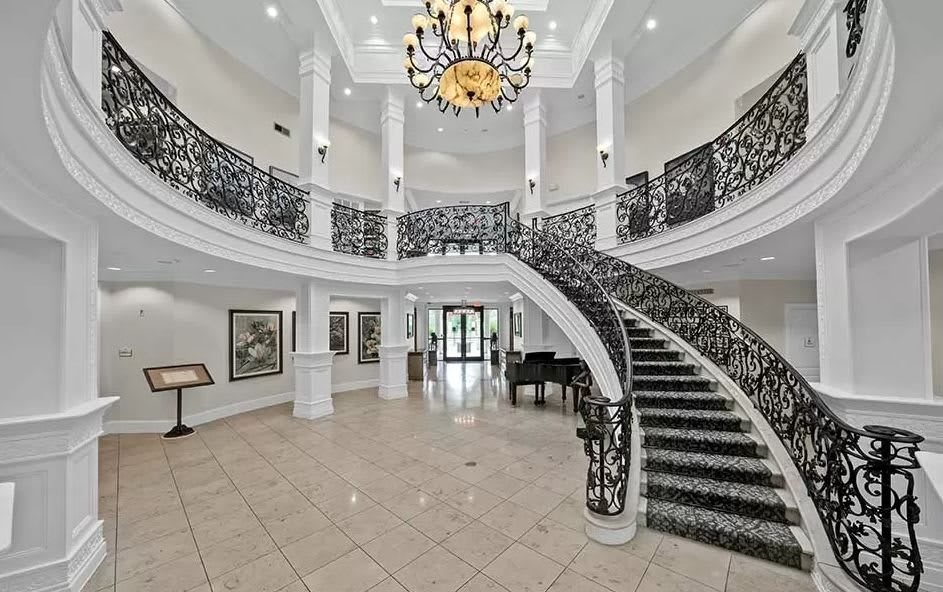 A luxurious foyer featuring a grand staircase with ornate railings and a large chandelier.