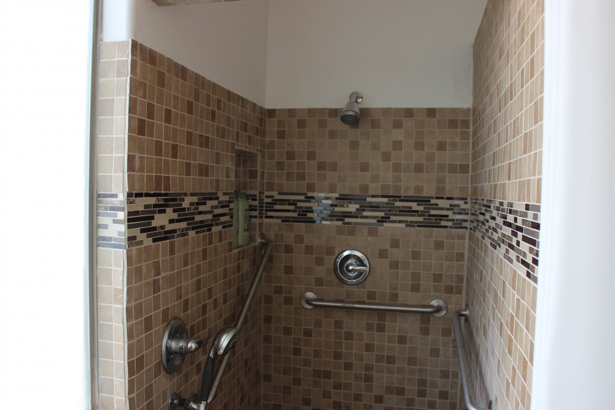 A tiled shower area with grab bars and a built-in shelf.