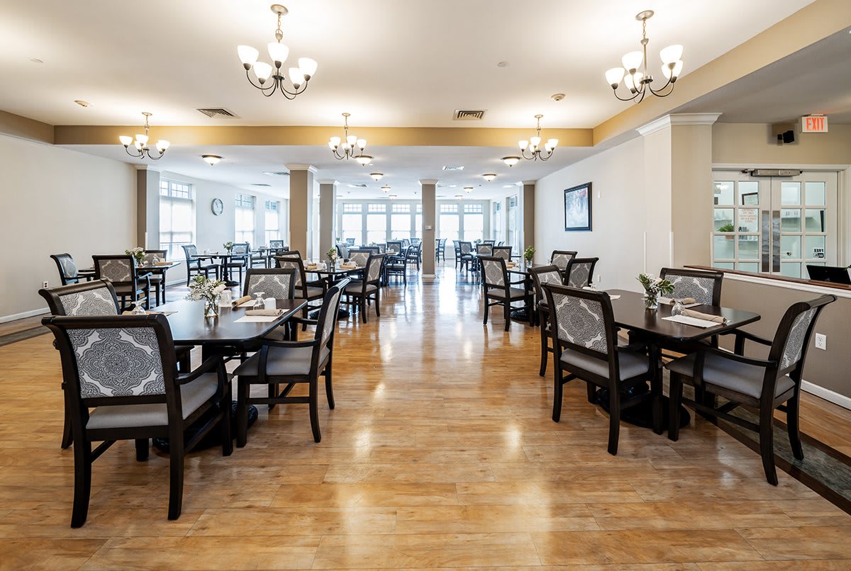 Spacious dining area with elegantly arranged tables and chairs, featuring chandeliers and wood flooring.