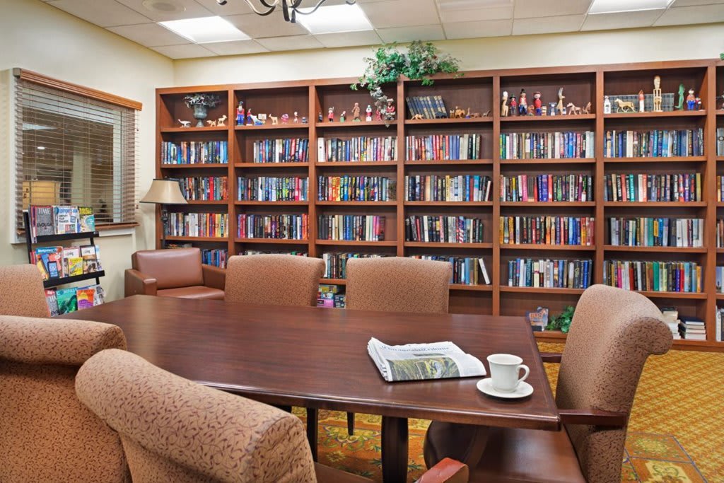 A cozy library room with bookshelves and a central table surrounded by chairs.