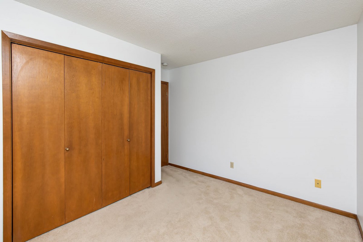 An empty room featuring white walls, a carpeted floor, and wooden closet doors.