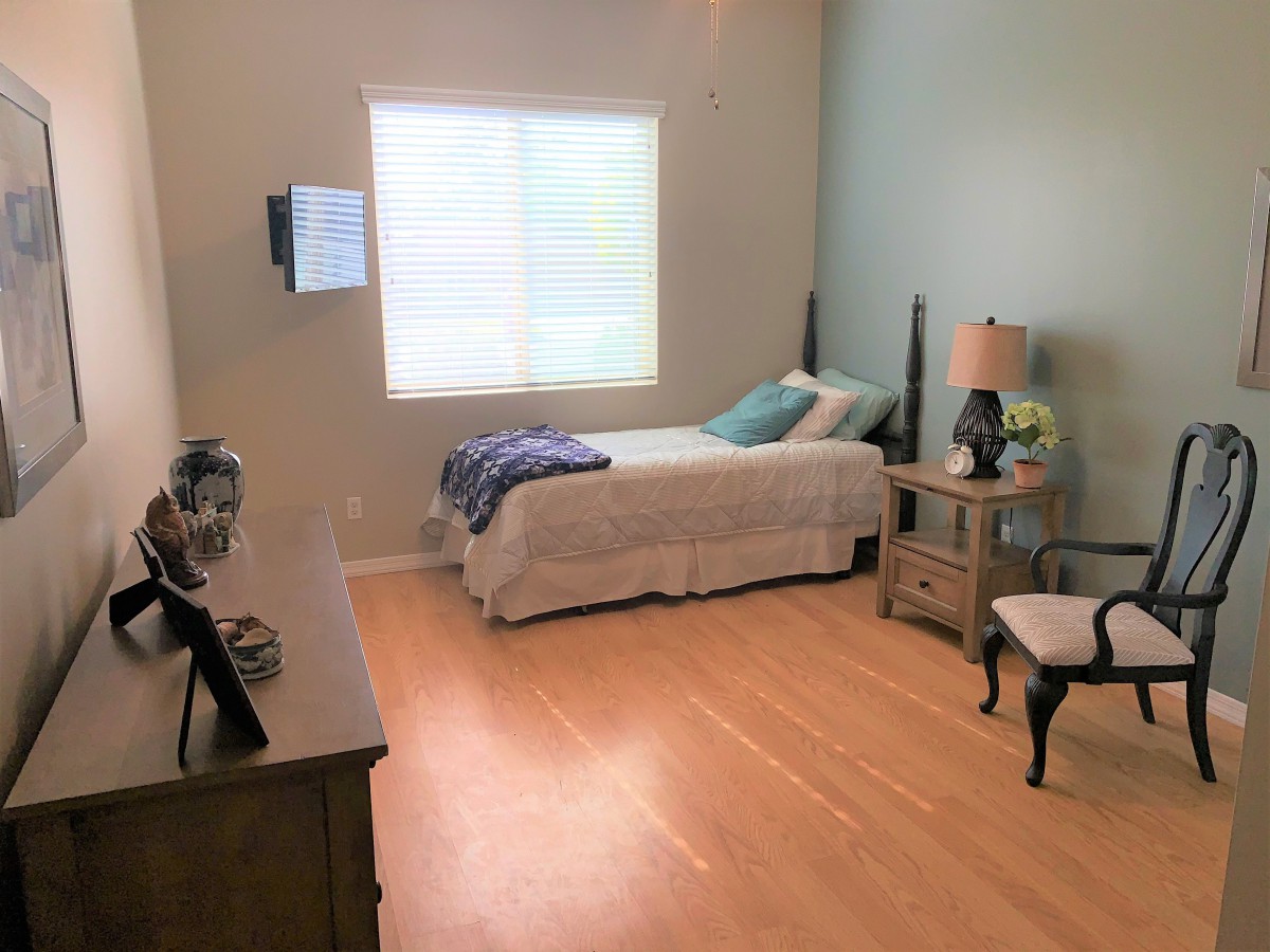 A minimalist bedroom with a single bed, a lamp, and a chair near the window.