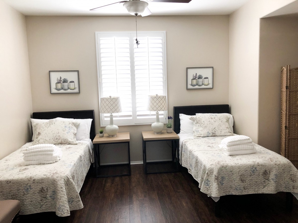 A tidy bedroom with twin beds, featuring matching lamps and artwork on the walls.