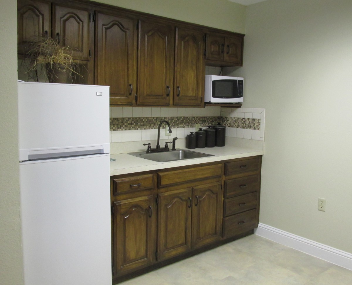 A small kitchen with wooden cabinets, a white refrigerator, microwave, sink, and countertop.