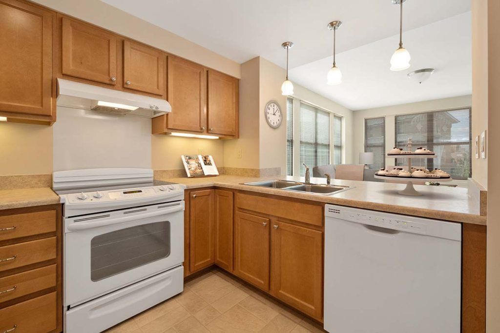 A modern kitchen with wooden cabinets, featuring a stove, dishwasher, and pendant lighting.
