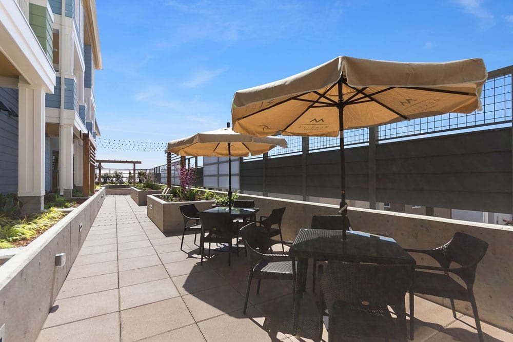 A sunny outdoor patio with tables, chairs, and umbrellas.