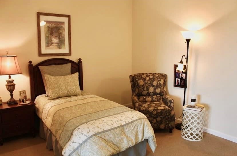 A cozy bedroom with a single bed, floral armchair, and standing lamp.