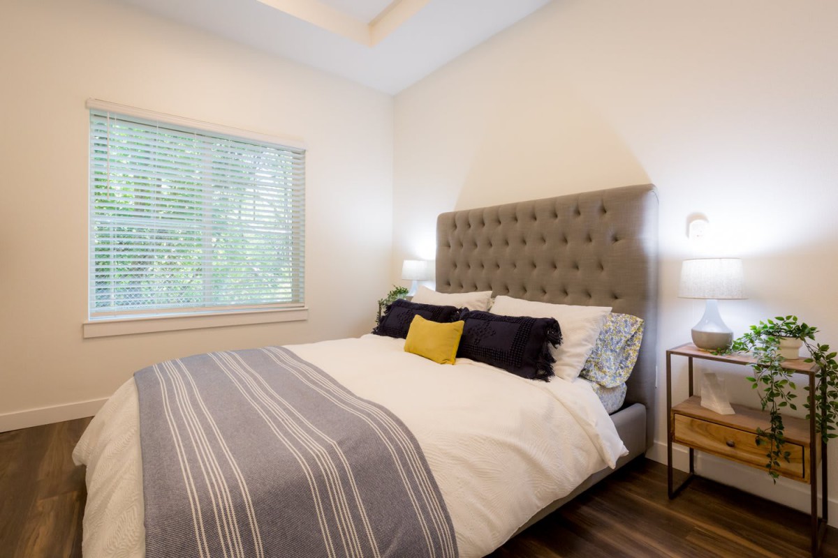 A modern bedroom with a tufted headboard, stylish bedding, and ample natural light through a window.
