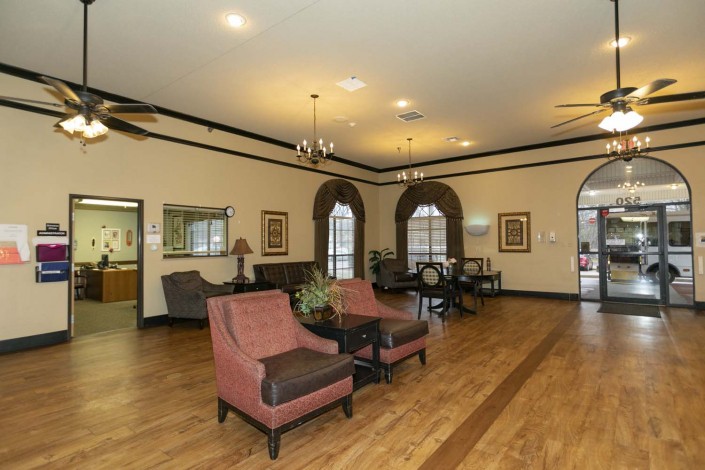 A spacious lobby with elegant furniture and chandeliers, featuring wooden flooring and large windows.