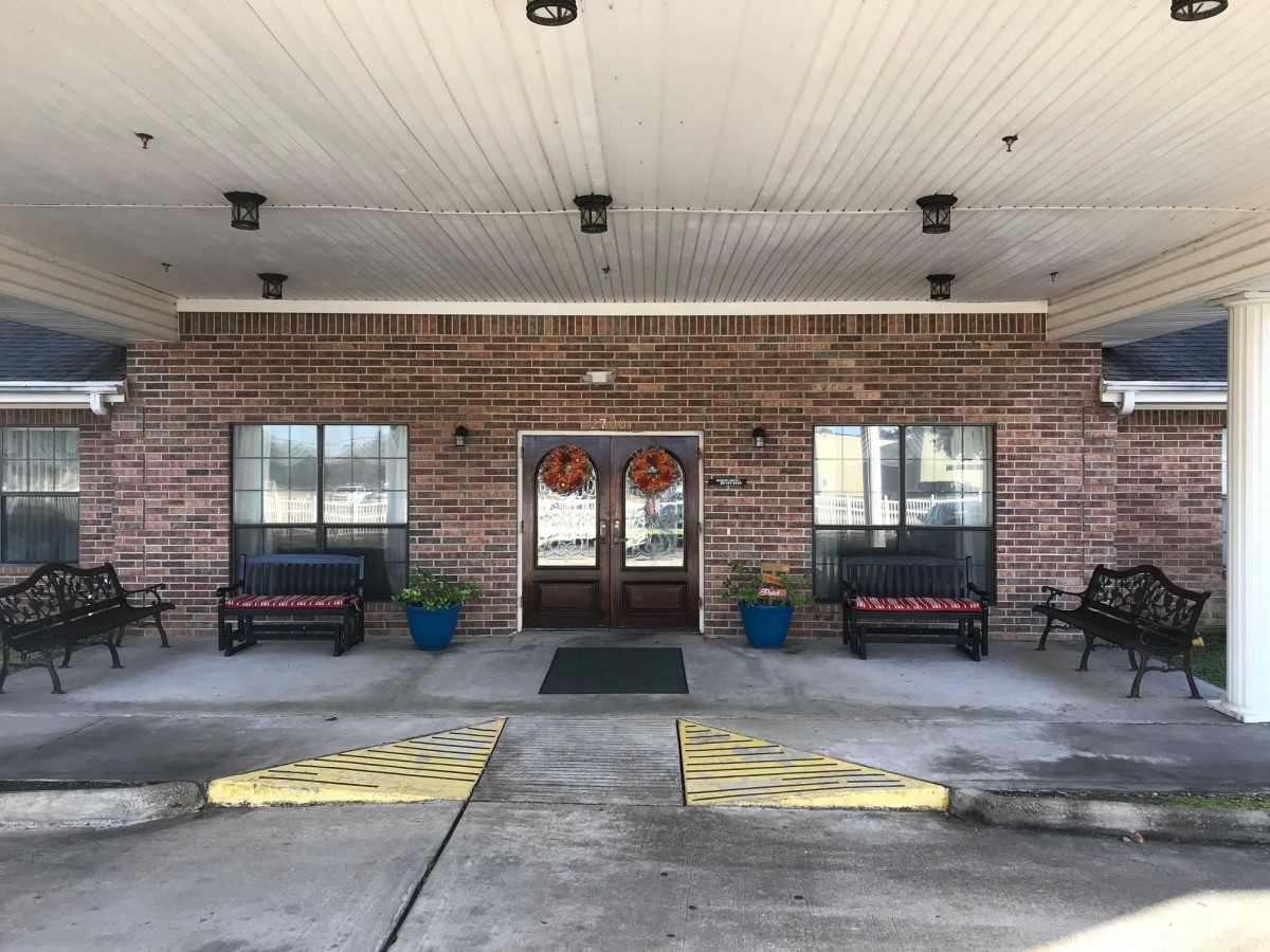 The entrance features a brick exterior with double doors, flanked by benches and potted plants.