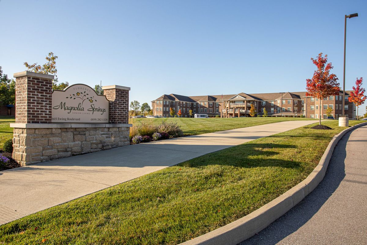 A view of a residential apartment complex with a large green lawn and a welcoming driveway entrance.