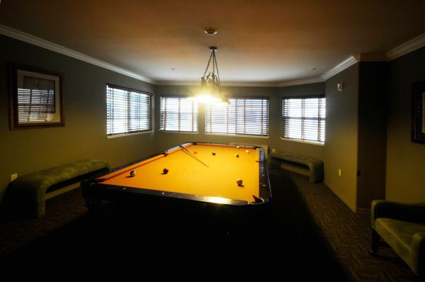 A dimly lit pool room with a billiard table and surrounding windows.