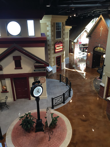 A charming indoor model village featuring a central clock and various shop facades.