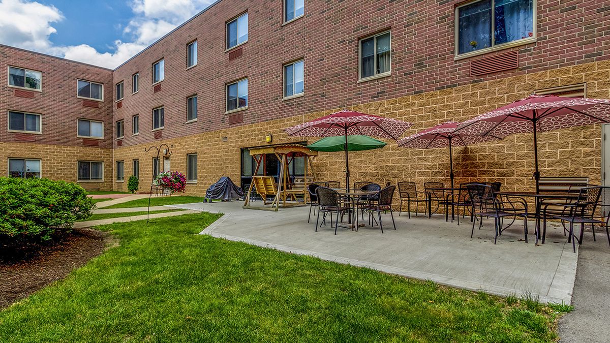 An outdoor patio area with tables, chairs, and umbrellas adjacent to a brick building.