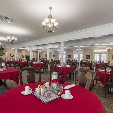 An elegant dining room featuring tables with red tablecloths and chandeliers.