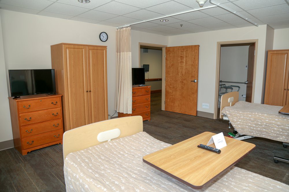 A hospital room with beds, wardrobes, and a television.