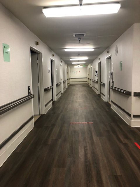 A long, well-lit hospital corridor with several doors on either side.