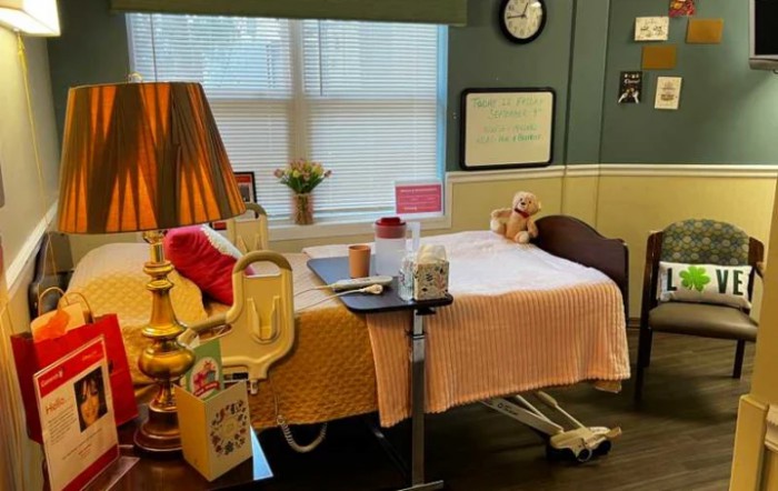 A cozy hospital room with a decorated bed, a lamp, and a teddy bear by the window.