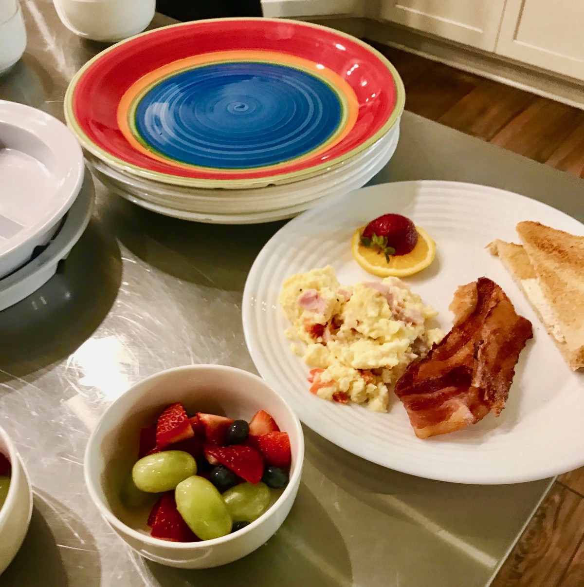 A breakfast spread featuring scrambled eggs, bacon, and toast with a side of fresh fruit.