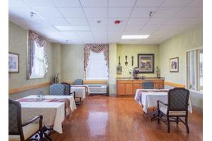 A well-lit dining area with tables and chairs, featuring decorative curtains and artwork on the walls.