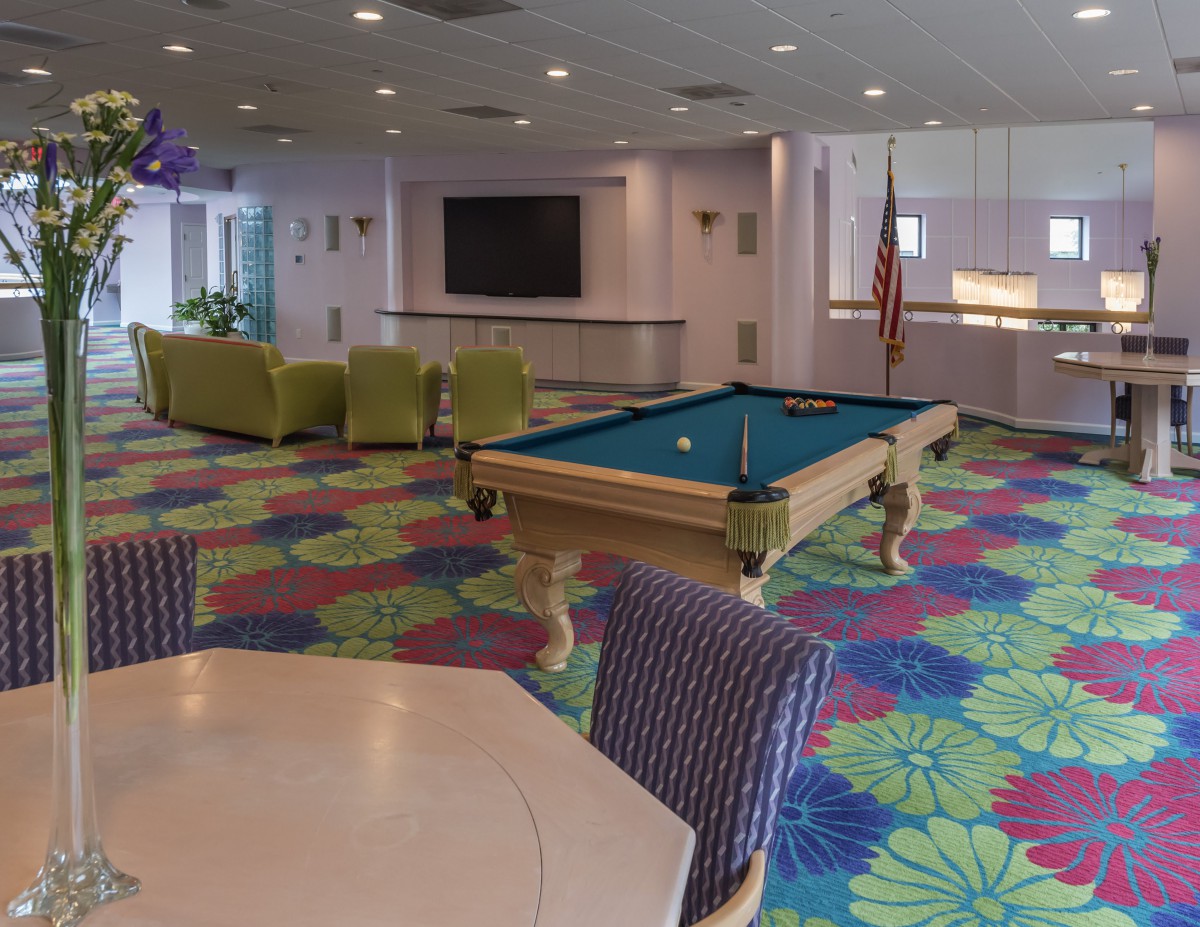 A vibrant recreation room featuring a pool table, colorful carpet, and a seating area with a television.