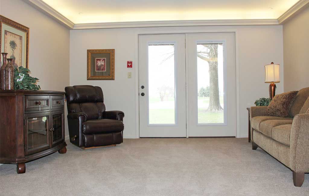 A cozy living room features a recliner, artwork on the wall, and large glass doors overlooking the outside.