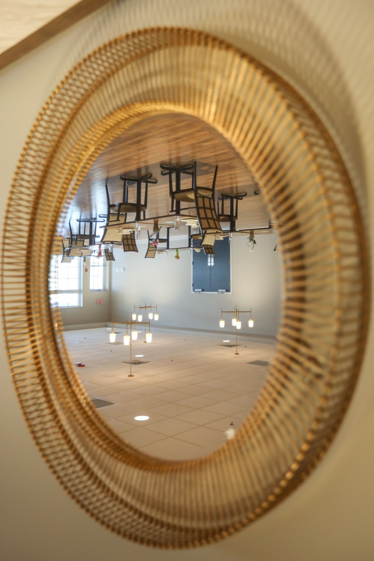 A room with chairs and lights reflected upside down in an oval mirror.