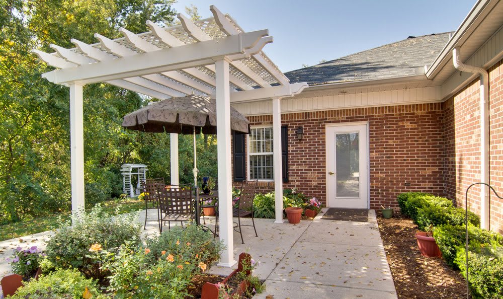 A cozy backyard patio with a pergola providing shade over outdoor seating, adjacent to a brick house.