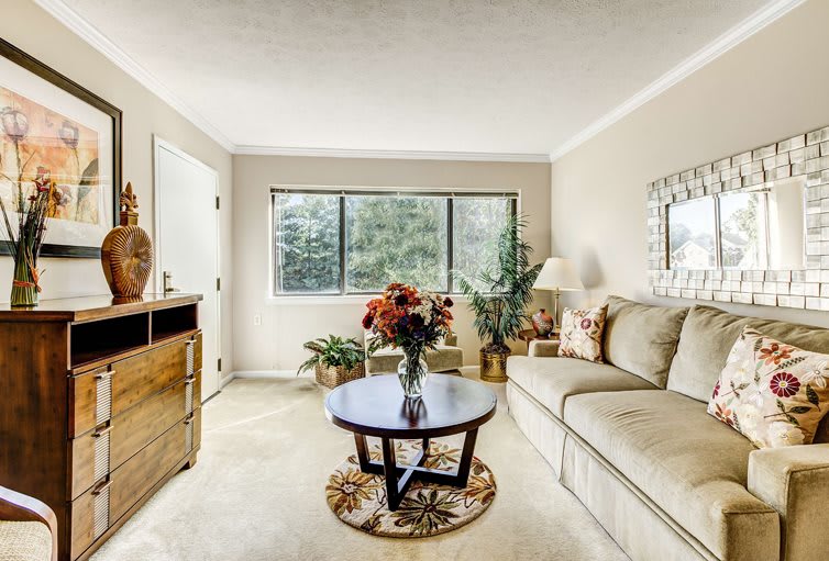 A cozy living room with a sofa, coffee table, and decorative elements including plants and flowers.