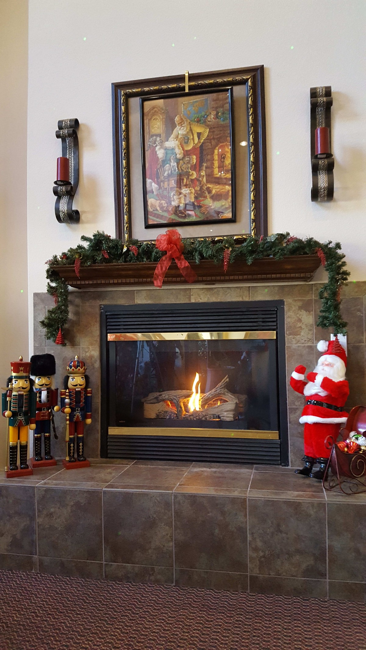 A cozy fireplace adorned with festive Christmas decorations, including a Santa Claus figure, nutcrackers, and garland.
