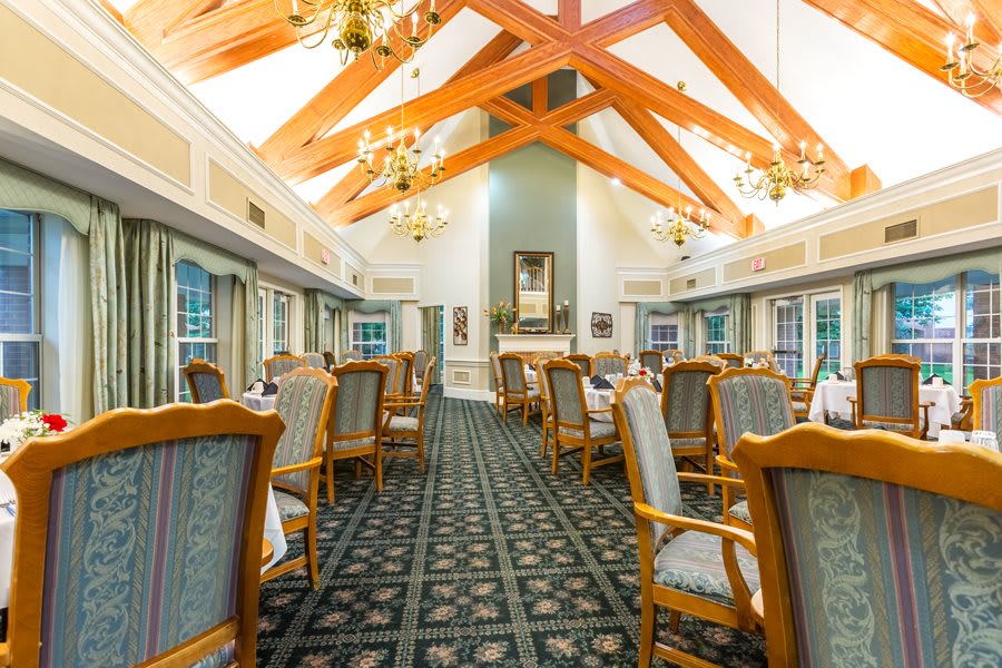 An elegant dining room with wooden beams, chandeliers, and neatly arranged tables and chairs.